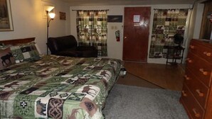 A bedroom with a large bed, a dresser, a chair, and a door leading to another room.