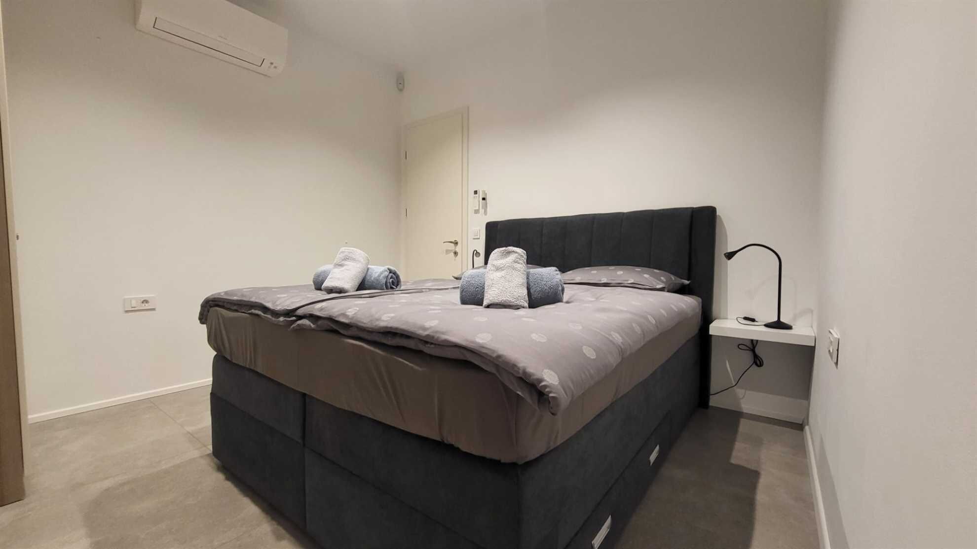 A modern bedroom with a bed, a bedside table, a lamp, and a wall-mounted air conditioner.