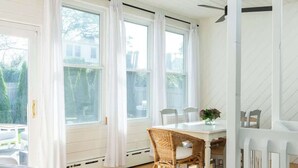 Una habitación con ventilador de techo, una mesa de comedor con sillas y vistas al exterior a través de amplios ventanales.