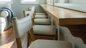 Una habitación con un banco de madera largo, varias sillas y ventanas grandes.