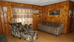 Een kamer met houten lambrisering, een bank, twee fauteuils en een kamerkleed met patroon.