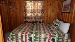 Een kamer met houten lambrisering, een bed met een geborduurde deken, een gordijn met dierenmotieven en een ingelijste foto aan de muur.