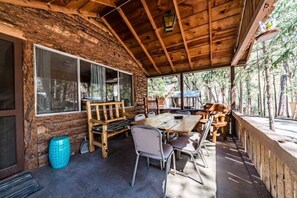 A rustic wooden cabin with a covered patio, furnished with a table and chairs, and large windows.