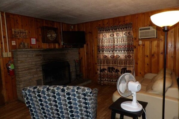 A cozy living room with a fireplace, patterned curtains, a clock, and a fan.