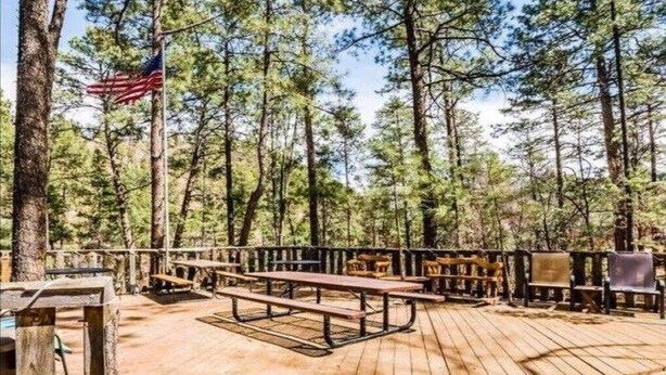 Eine Holzterrasse mit Picknicktischen und Bänken, umgeben von hohen Kiefern.