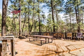 Guests can sit and enjoy the natural surroundings at this outdoor deck area, surrounded by tall pine trees and featuring picnic tables and benches.