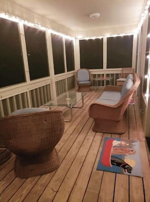 Un espacio al aire libre techado con mobiliario de mimbre, una mesa de vidrio y un tapete con ilustración de un perro.
