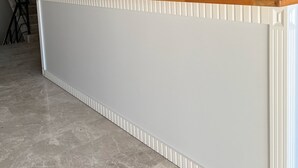 A reception desk with a modern design, featuring a grey wall with the hotel's name and logo. There are four pendant lights above the desk, and a staircase is visible in the background. - DADA OTEL (Ezine)