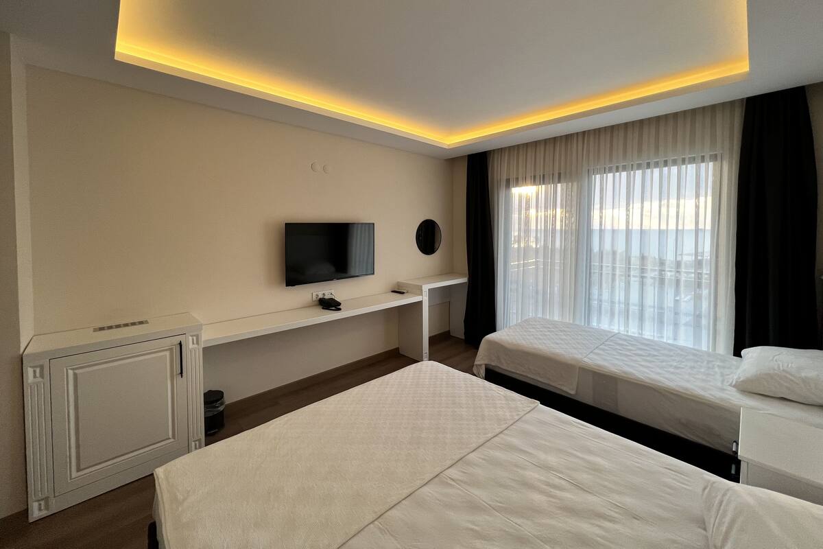 Habitación de hotel con dos camas, televisión montada en la pared, un escritorio y una ventana con cortinas.