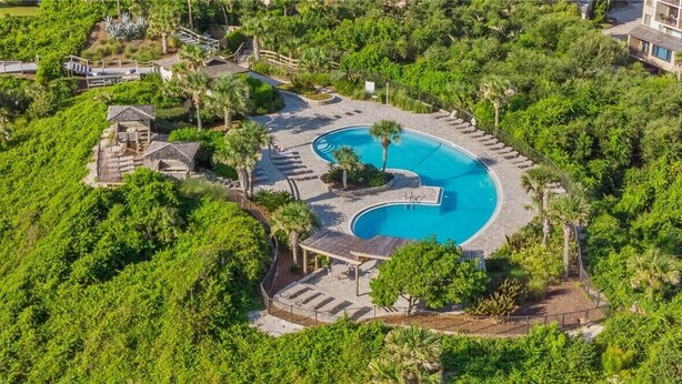Luchtbeeld van een resort met een groot zwembad, omringd door weelderige begroeiing en palmbomen.