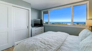 Een slaapkamer met een bed, een dressoir, een televisie op het dressoir en een raam met uitzicht op zee.