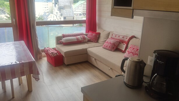 A cozy living area with a sofa, red cushions, a coffee maker, and a view of buildings through a window.