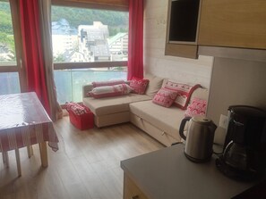Ein gemütlicher Wohnbereich mit einer Couch, roten Kissen, einer Kaffeemaschine und Blick auf Gebäude durch ein Fenster.