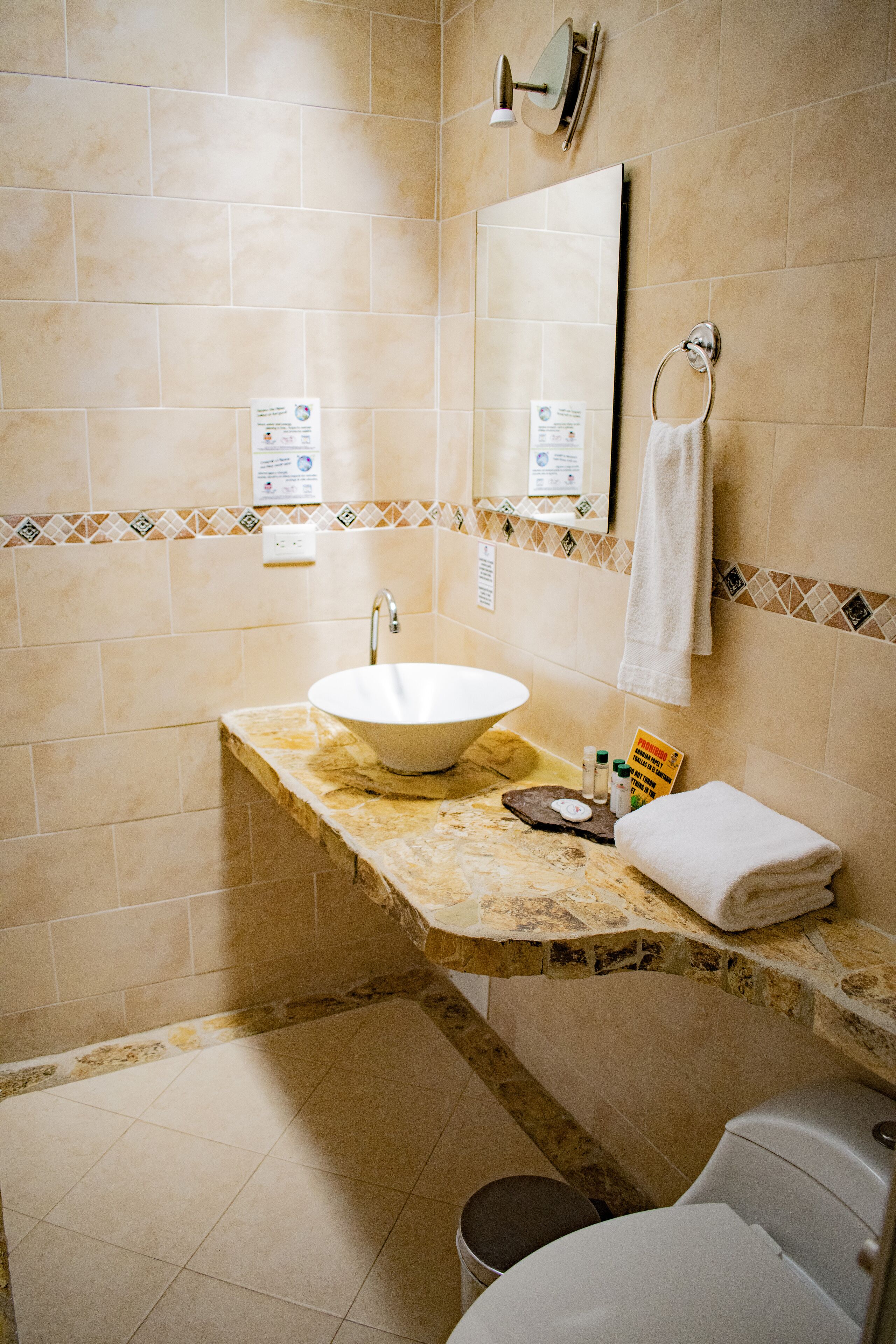 A bathroom with a white sink, a mirror, a towel ring, and a toilet.