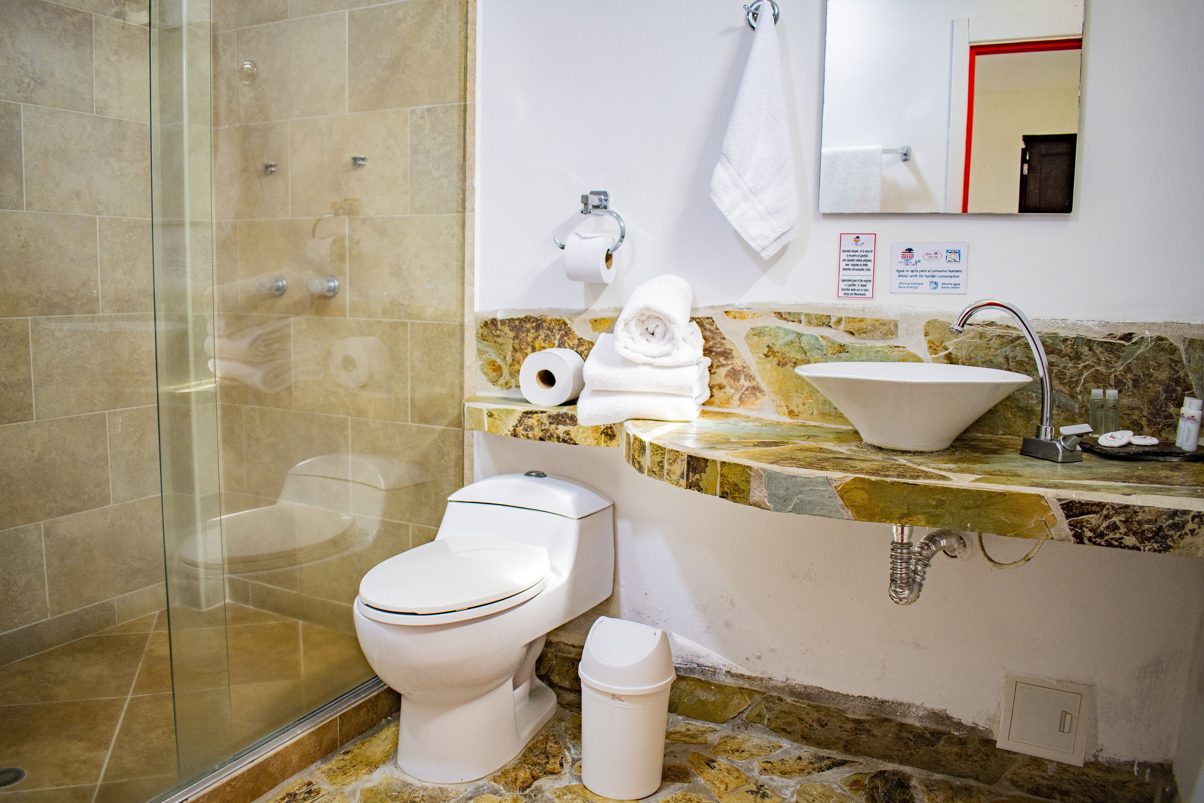 Une salle de bain dotée d’une douche à parois de verre, de toilettes, d’un lavabo avec un plan de travail en marbre et d’un miroir au-dessus du lavabo.