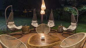 Ein runder Holztisch, umgeben von fünf Korbstühlen mit Kissen, auf einer gefliesten Terrasse.