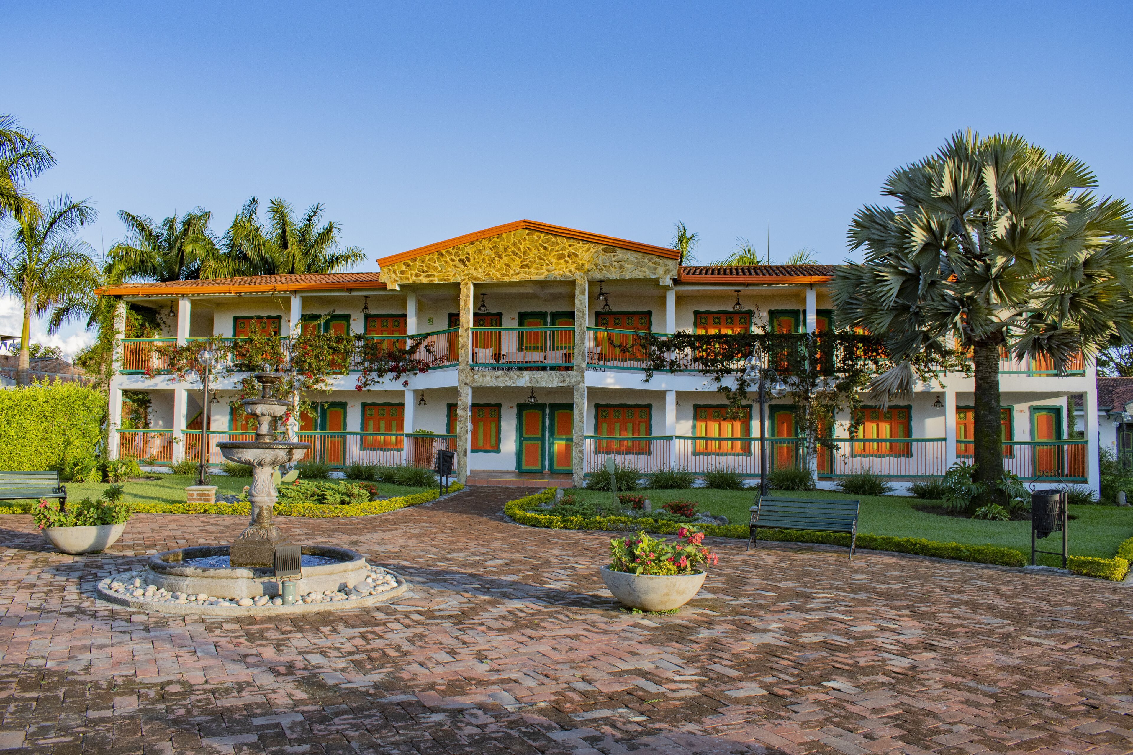 Un edificio de dos pisos con un patio, una fuente y un banco.