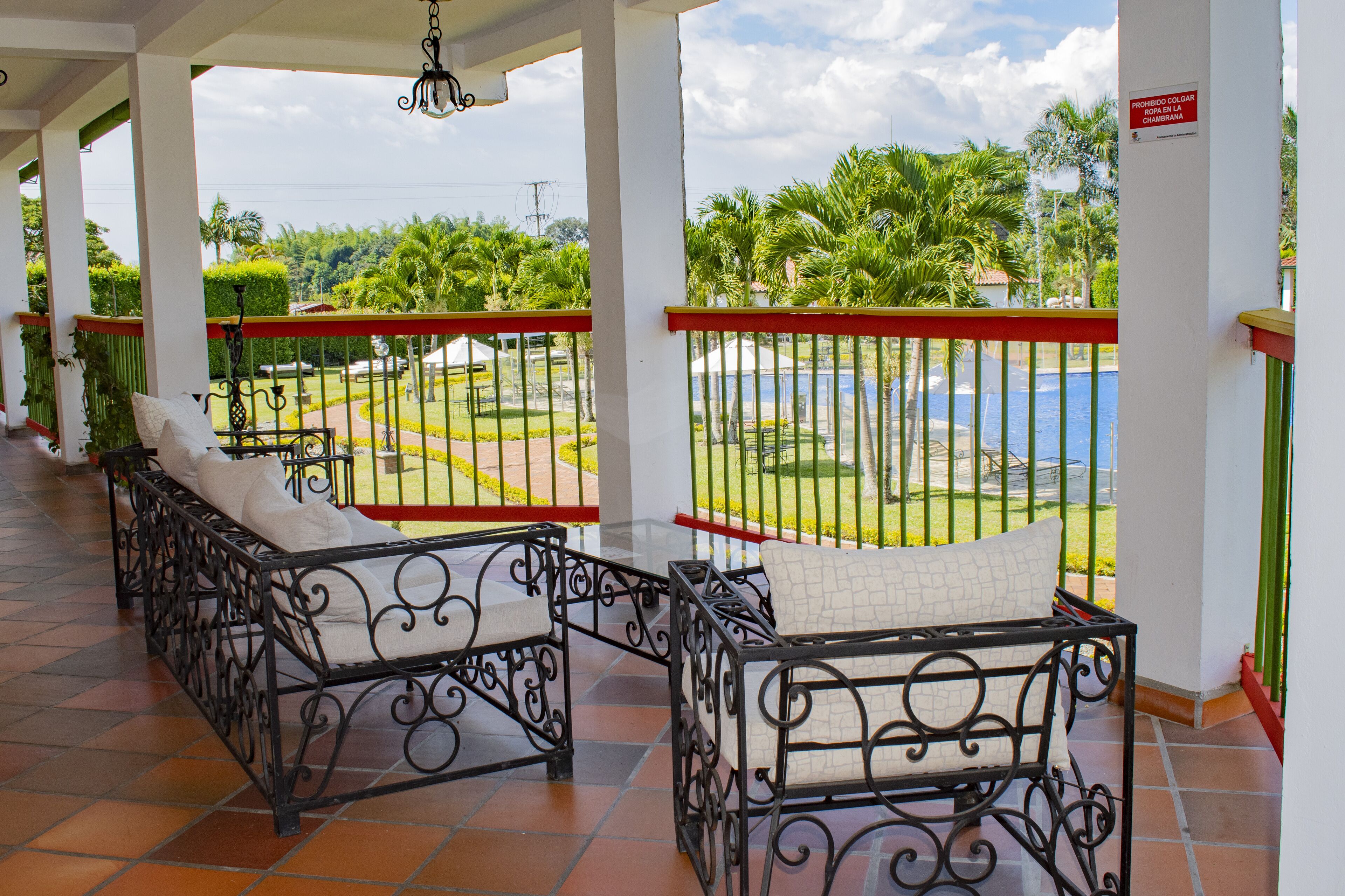 A covered balcony with wrought iron furniture and a view of a landscaped garden and pool.