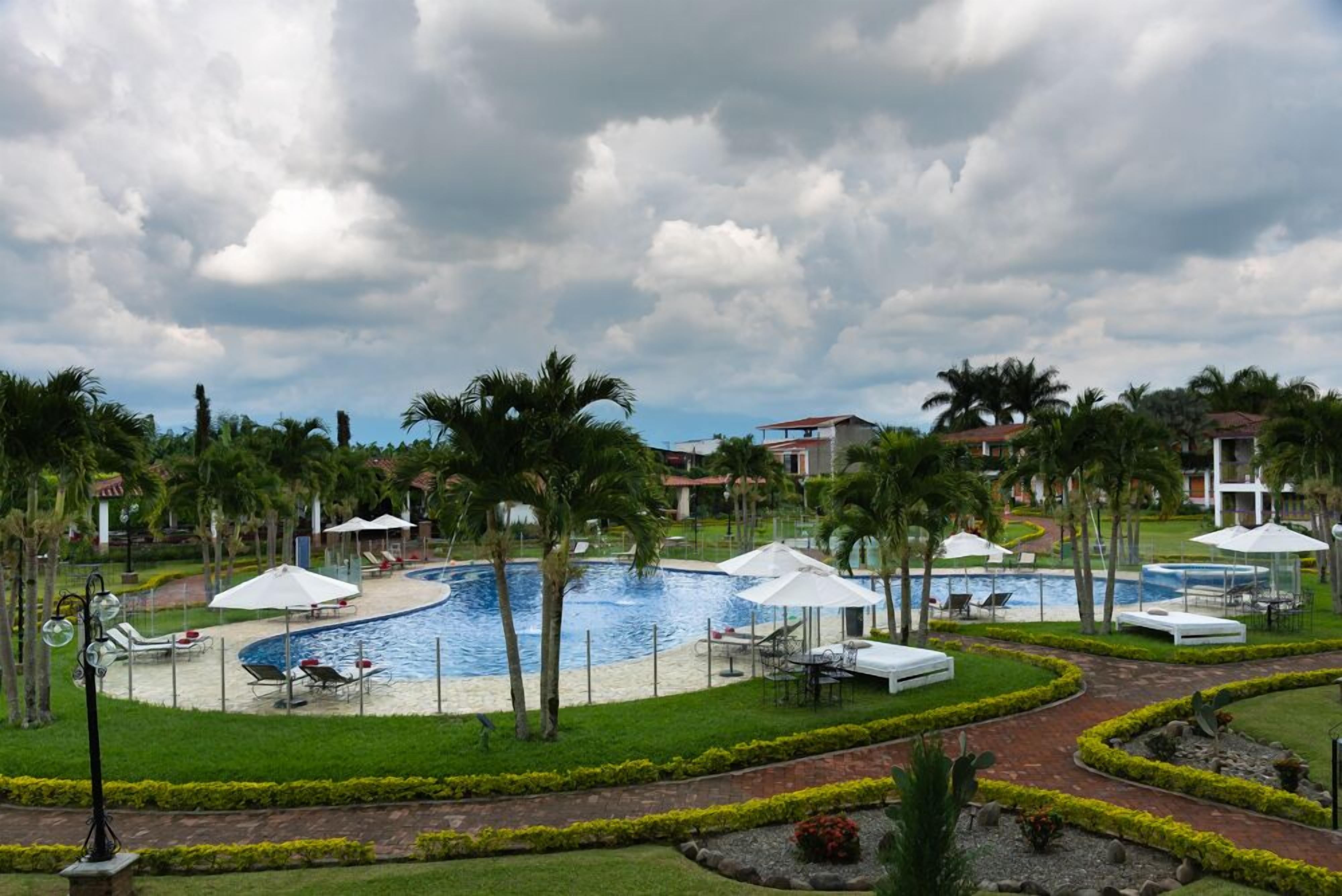 Un resort con piscina central, palmeras y sillas de descanso.