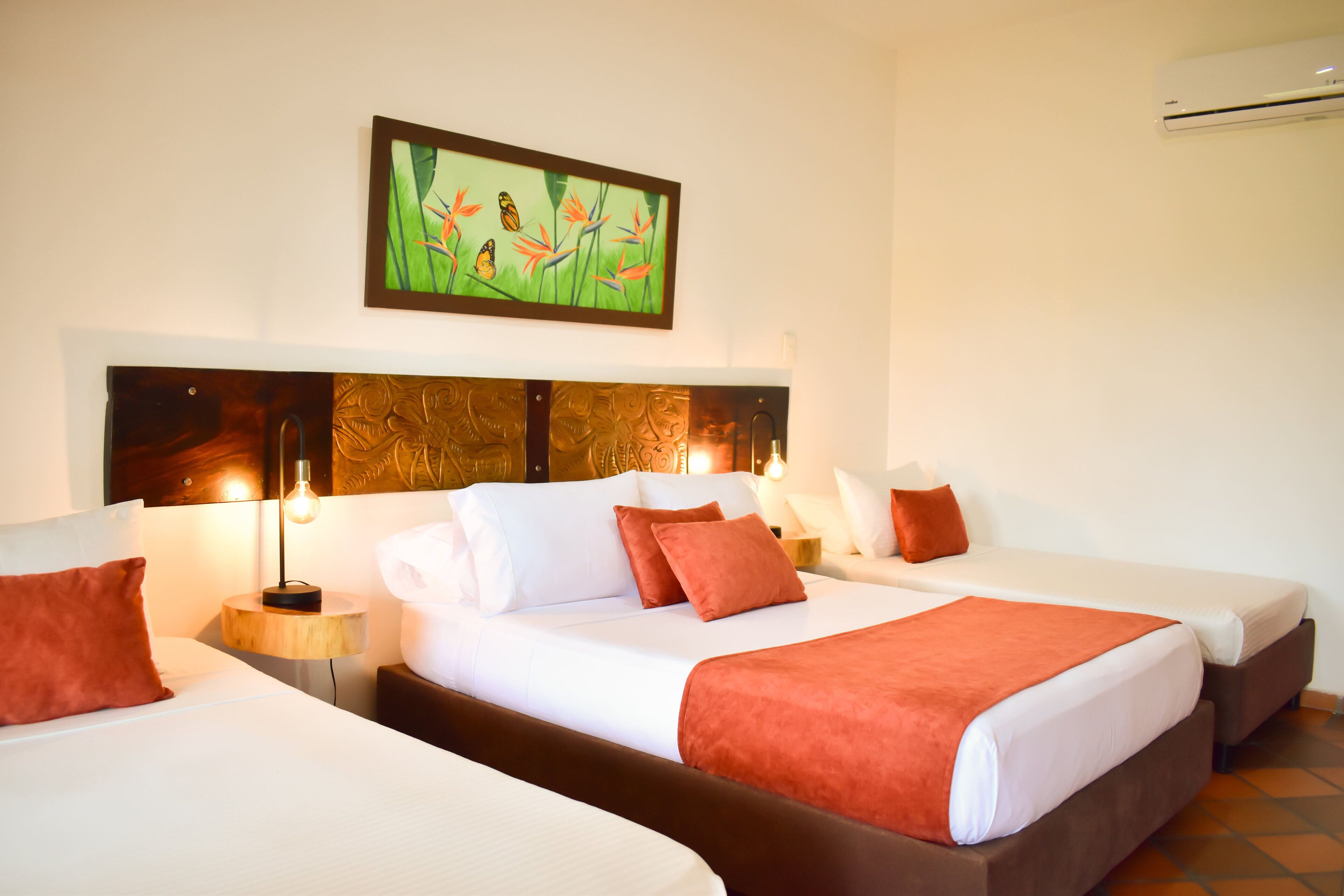 Habitación de hotel con dos camas, un cuadro grande sobre la cabecera y un equipo de aire acondicionado en la pared.