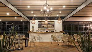 Uma área de bar ao ar livre com cadeiras de vime, balcão e um lustre.