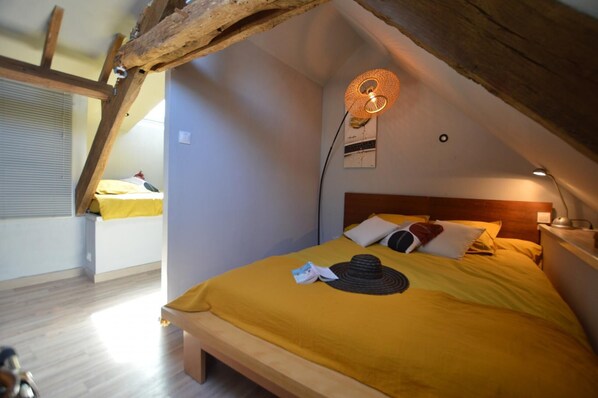 Un dormitorio acogedor con techo inclinado, cama con ropa de cama amarilla, cabecero de madera y lámpara fijada a la pared.
