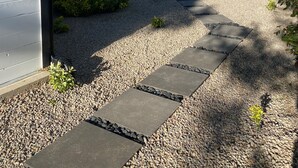Une maison moderne dotée d’un patio couvert, d’un chemin de gravier et d’un espace verdoyant tout autour.