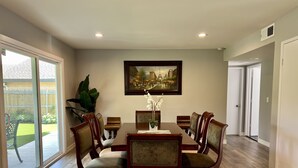 Comedor con mesa de madera, seis sillas, un cuadro enmarco y una planta en maceta.