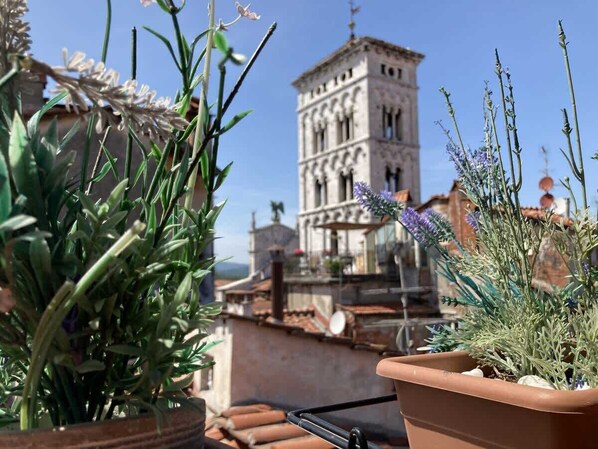 A terrace with potted plants and a view of a historic tower.