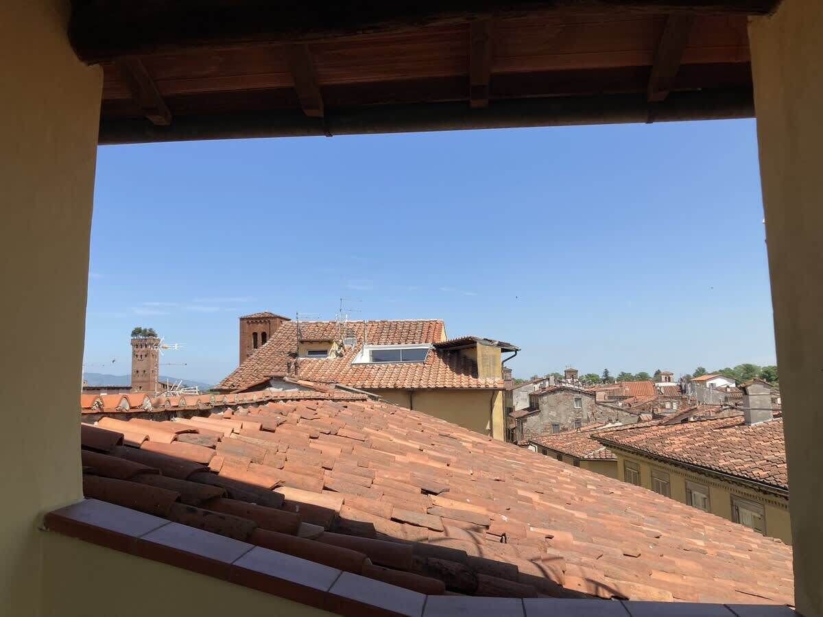 Une vue depuis une fenêtre donnant sur des toits couverts de tuiles en terre cuite et sur une tour historique.