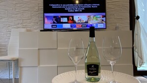 Ein Hotelzimmer mit einem flachbildfernseher an einer strukturierten Wand, einem Tisch mit einer Weinflasche und zwei Gläsern sowie einem weißen Stuhl.