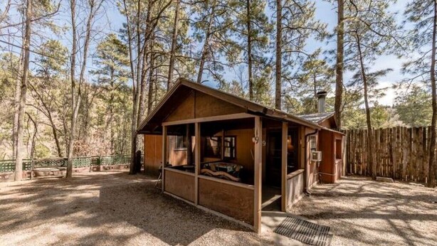 Un chalet rustique doté d’un porche abrité, entouré de grands pins.