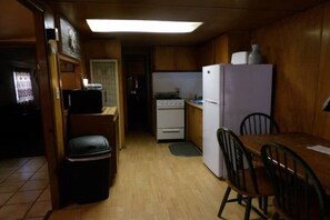 A compact kitchen with wooden cabinets, a white refrigerator, a stove, and a small dining area with a table and chairs.
