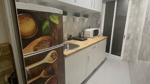 A modern kitchen with white cabinets, a microwave, and a sink. There are potted plants on the countertop and a refrigerator with a food-themed door.