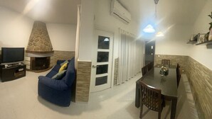 A living room with a stone fireplace, a sofa, a TV, and a dining area with a table and chairs.