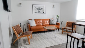 Ein modernes Wohnzimmer mit einem Ledersofa, Holzstühlen, einem Couchtisch und einem kleinen Beistelltisch.