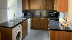 A modern kitchen with wooden cabinets, a washing machine, a microwave, and a sink. - Charming Stone Parlour Cottage set in an area of outstanding beauty. (Biggar)