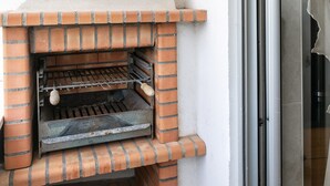 A brick-built outdoor oven with a metal door, positioned against a wall next to a sliding glass door. - Solange' Place - 300 metres from Nazaré Beach (Nazaré)