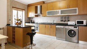 A modern kitchen with wooden cabinets, stainless steel appliances, and a central island with a black bar stool. - Solange' Place - 300 metres from Nazaré Beach (Nazaré)