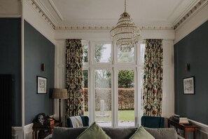A room with a large window, a chandelier, and a sofa with pillows.