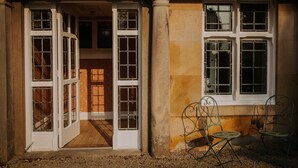 A building entrance with a set of double doors, a small outdoor seating area with two chairs, and a window with multiple panes. - The Pheasant Lodge - Spacious, luxury home with Garden Views & Log fire (Grange-over-Sands)