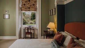 A bedroom with a bed, a desk, a chair, a lamp, and a window with a view of greenery. - The Pheasant Lodge - Spacious, luxury home with Garden Views & Log fire (Grange-over-Sands)
