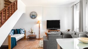 Ein modernes Wohnzimmer mit Treppe, einem Flachbildfernseher, einer Couch, einem Esstisch und einer Wanduhr.