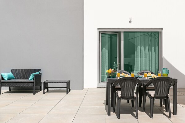 An outdoor patio with a sofa, a table set for four, and a sliding glass door leading to a balcony.