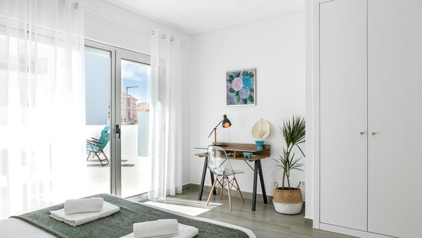 Moderni hotellihuone, jossa on sänky, työpöytä, tuoli, ruukkukasvi ja näkymä kaupunkiin.