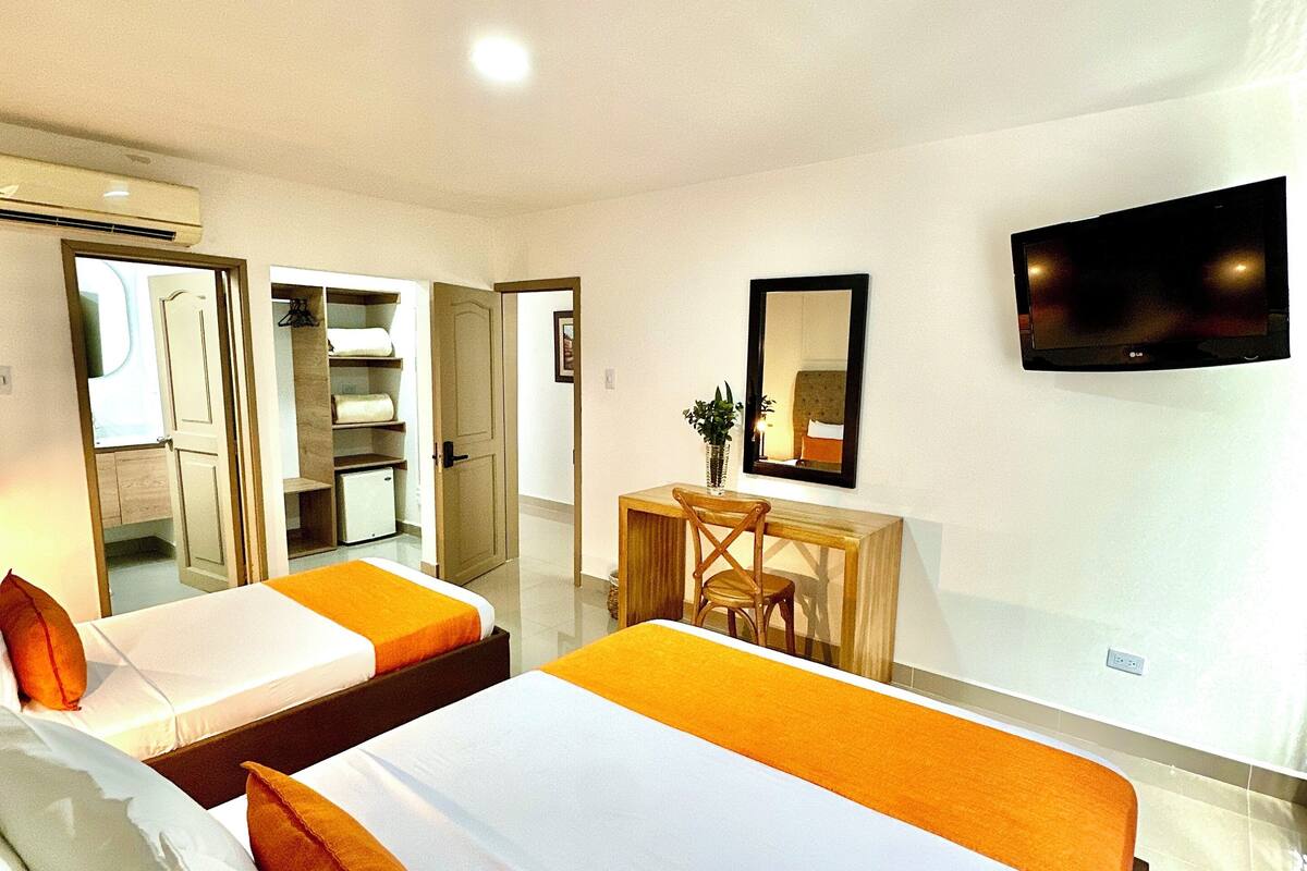A hotel room with two beds, a desk, a chair, a TV, and a mirror.