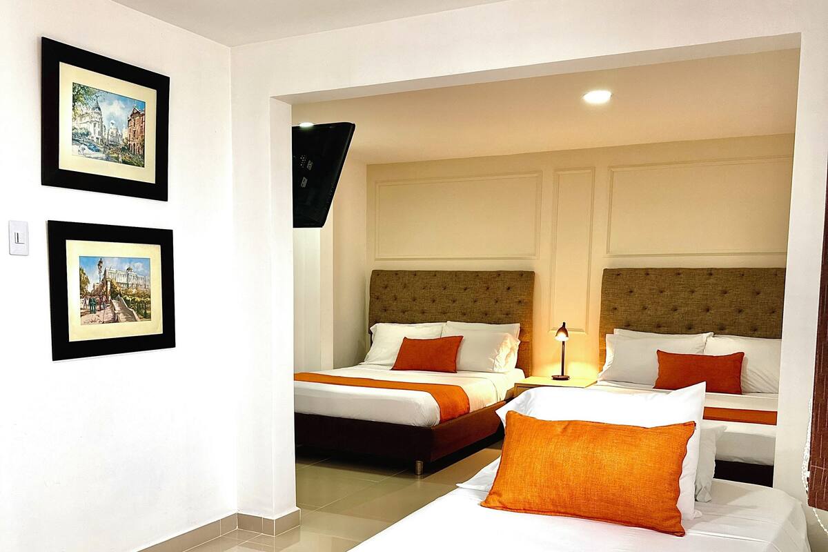 A hotel room with two beds, each with white and orange bedding, and a large window.
