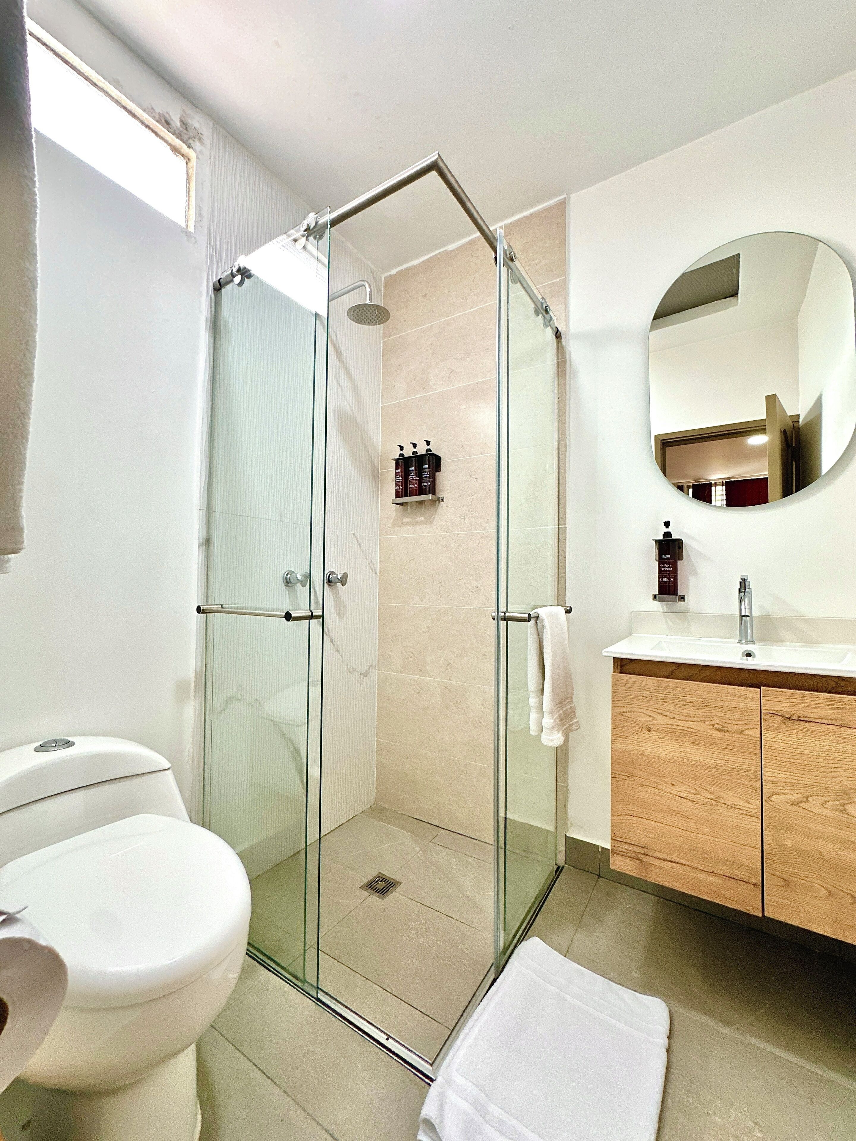 A modern bathroom with a glass-enclosed shower, a white toilet, a wooden vanity, and a large mirror.