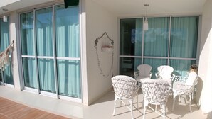 A balcony with white chairs and a table, large windows with curtains, and a hanging plant. - Conforto p/ 7 Hóspedes: Ar, Piscina e Praia (Barra de São Miguel)