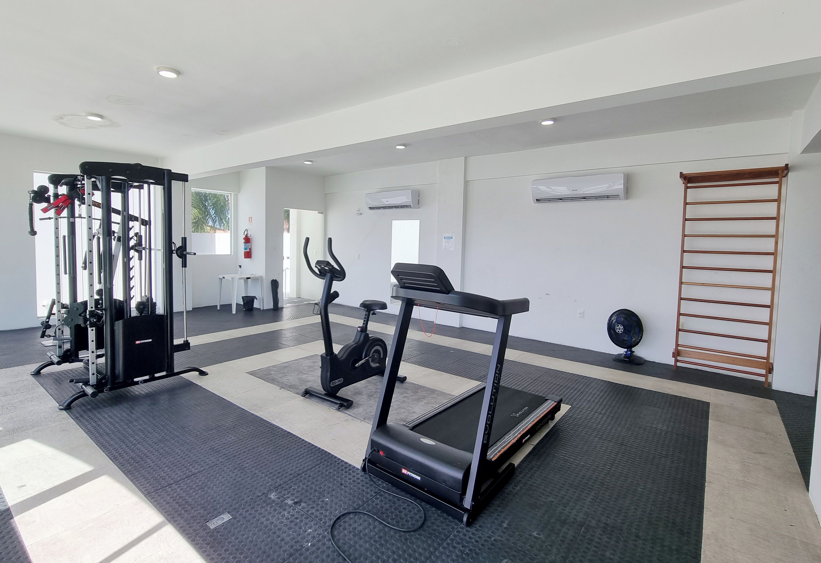 A gym with exercise equipment, a treadmill, and a wall-mounted fan.